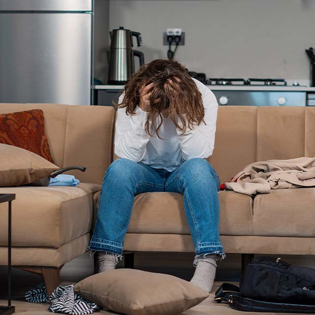 En person sitter i en soffa och håller sitt huvud i händerna.
